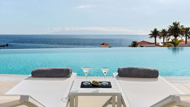 A poolside lounge with two lounge chairs, a tray with two martini glasses and a bowl of olives, and a view of the ocean and palm trees. - Landmar Playa La Arena (Santiago del Teide)