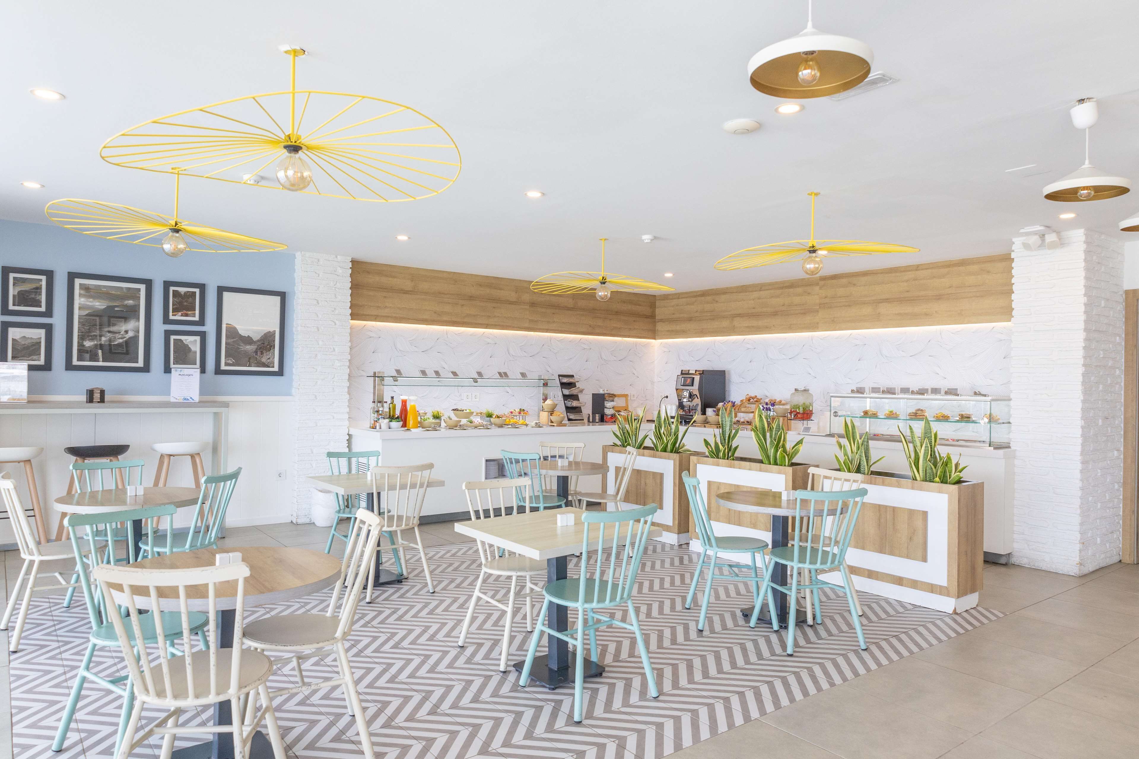 A modern restaurant interior with round tables, light blue chairs, and yellow pendant lights.