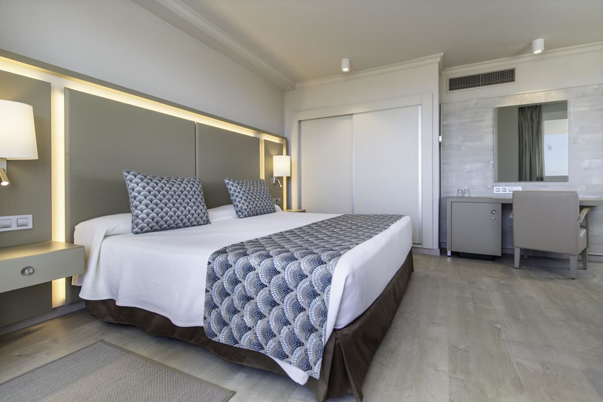 Een moderne hotelkamer met een groot bed, bedlampjes, een bureau en een spiegel.