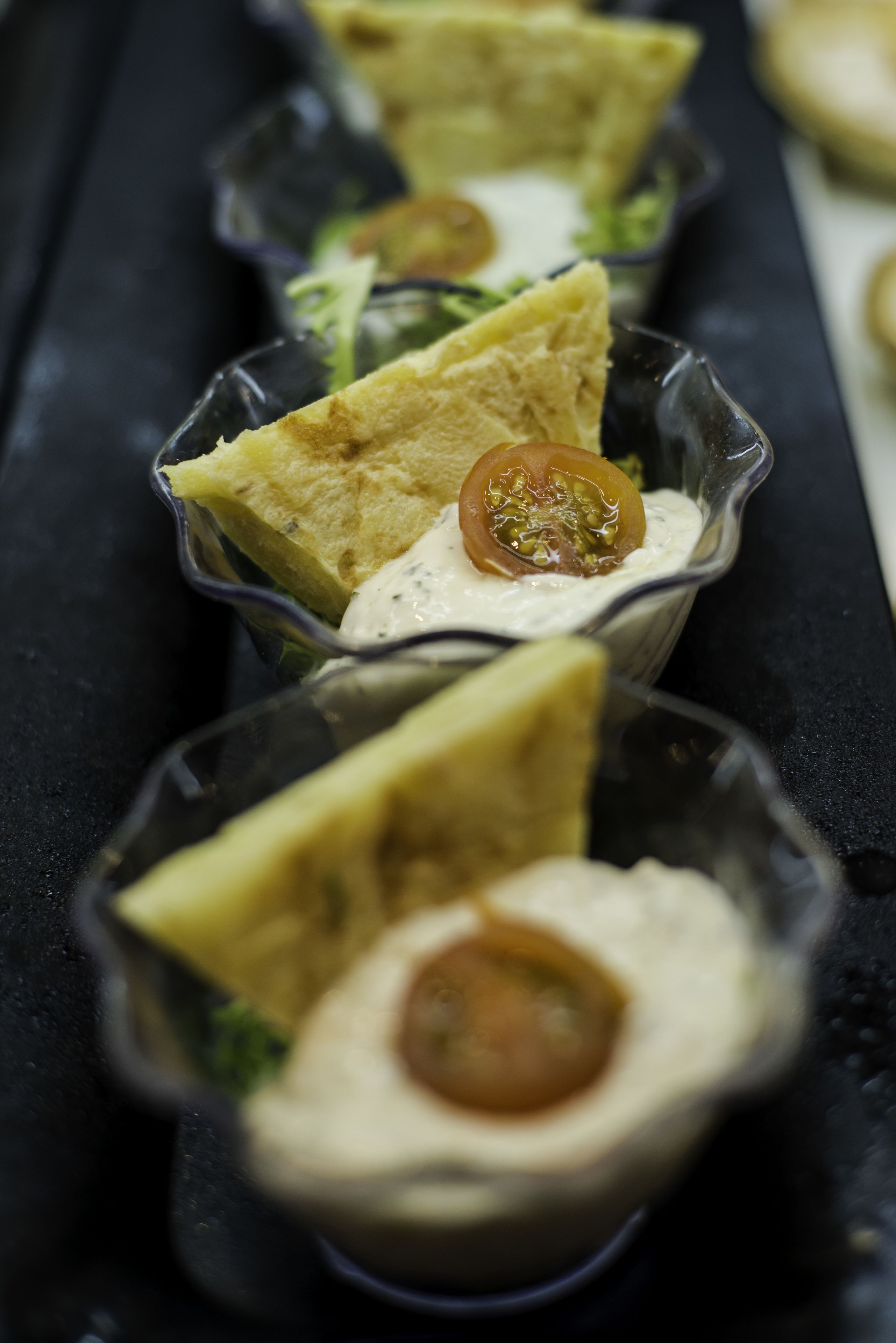 Una hilera de pequeños recipientes de vidrio con alimentos, probablemente aperitivos o bocadillos, sobre una superficie negra.