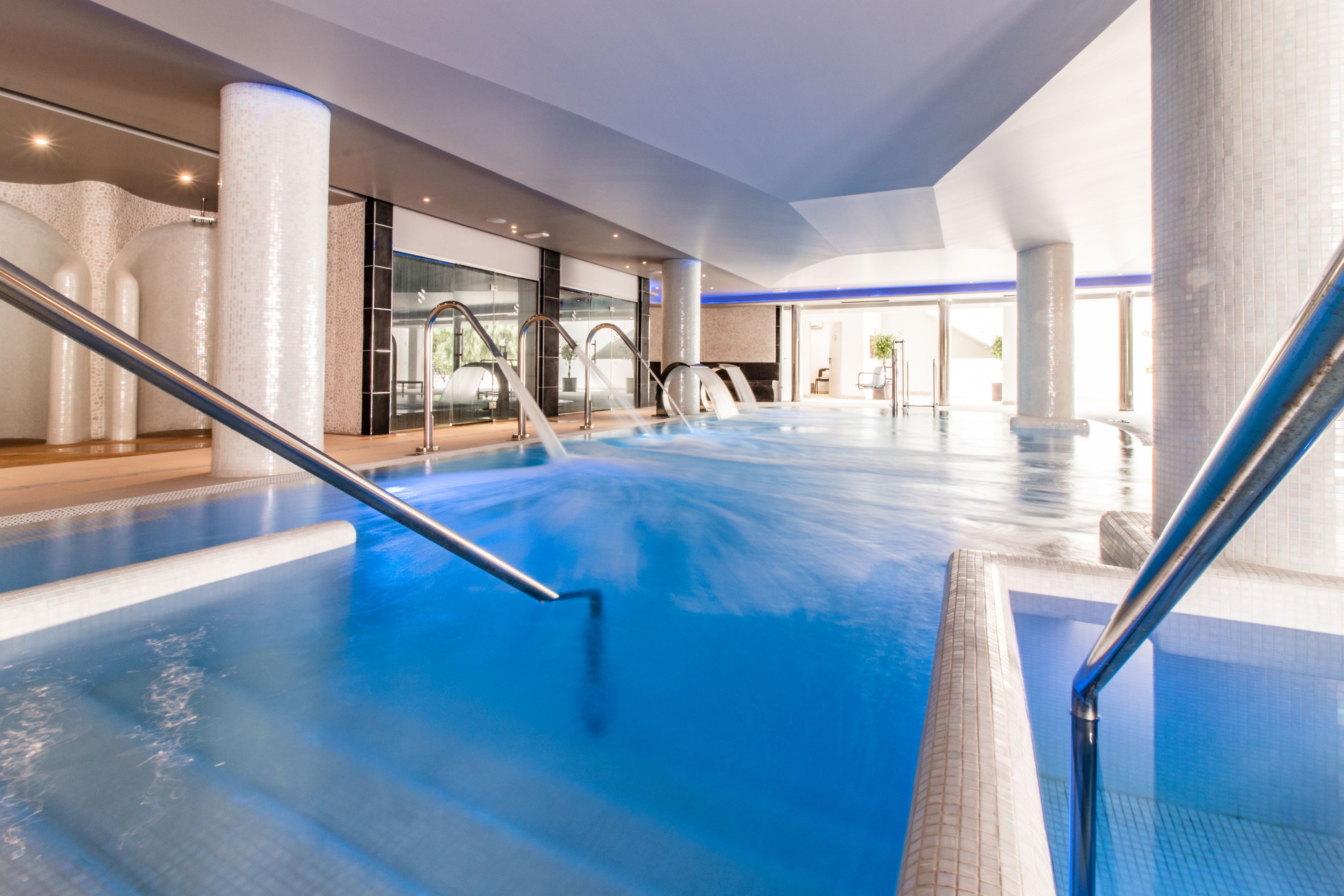Una piscina interior con agua cristalina, barandillas metálicas y un diseño arquitectónico moderno con amplios ventanales y columnas.