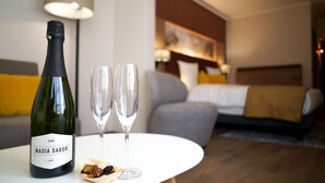 A hotel room with a bed, a white table with a wine bottle and glasses, and a lamp in the background. - Leonardo Hotel Antwerp (Antwerp)