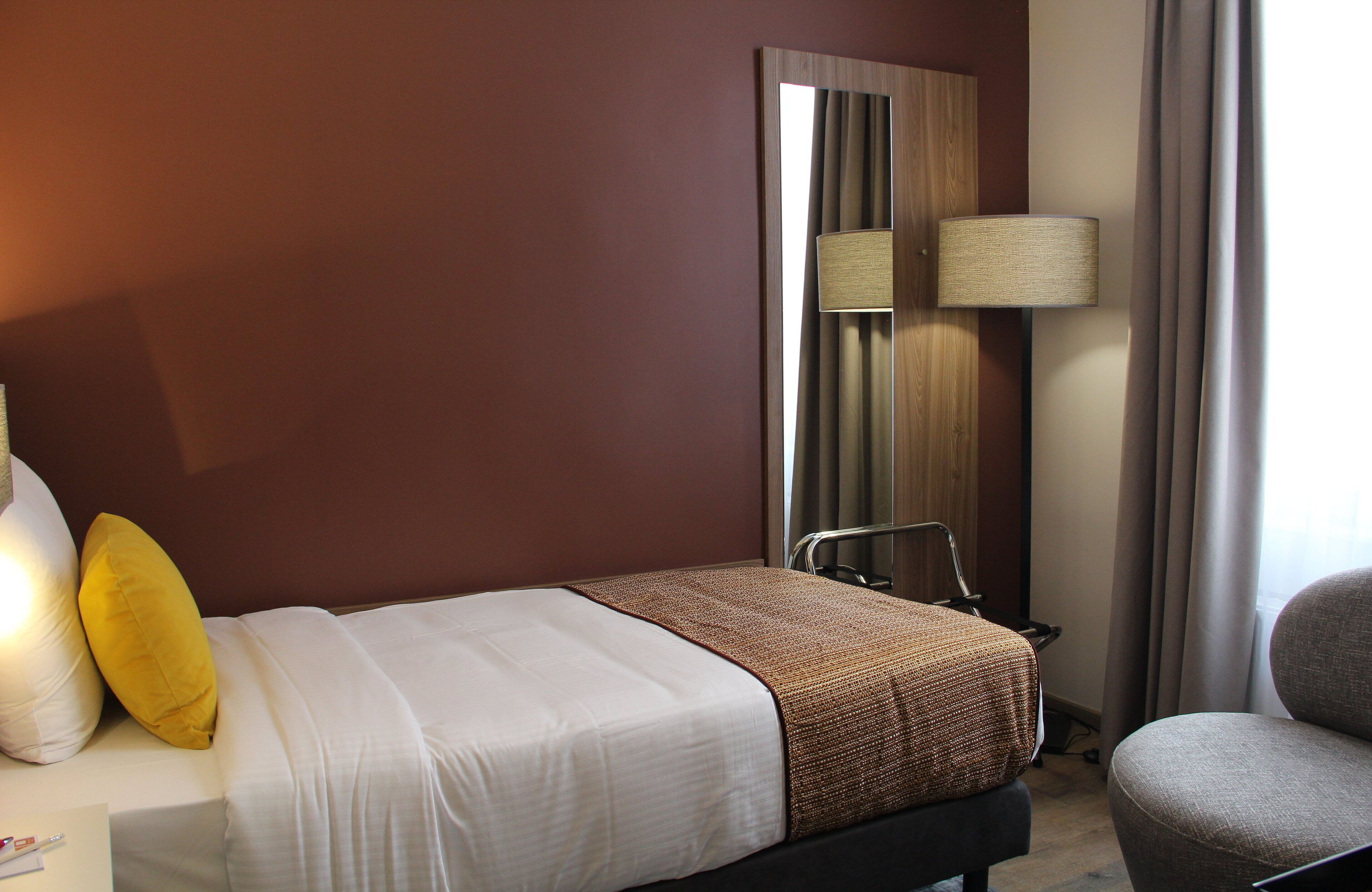 A hotel room with a bed, a chair, a lamp, and a mirror.