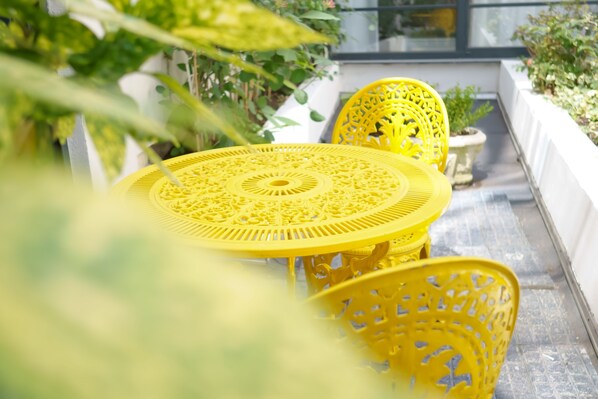 A yellow outdoor seating area with a round table and chairs, surrounded by potted plants and a white wall. - Leonardo Hotel Antwerp (Antwerp)
