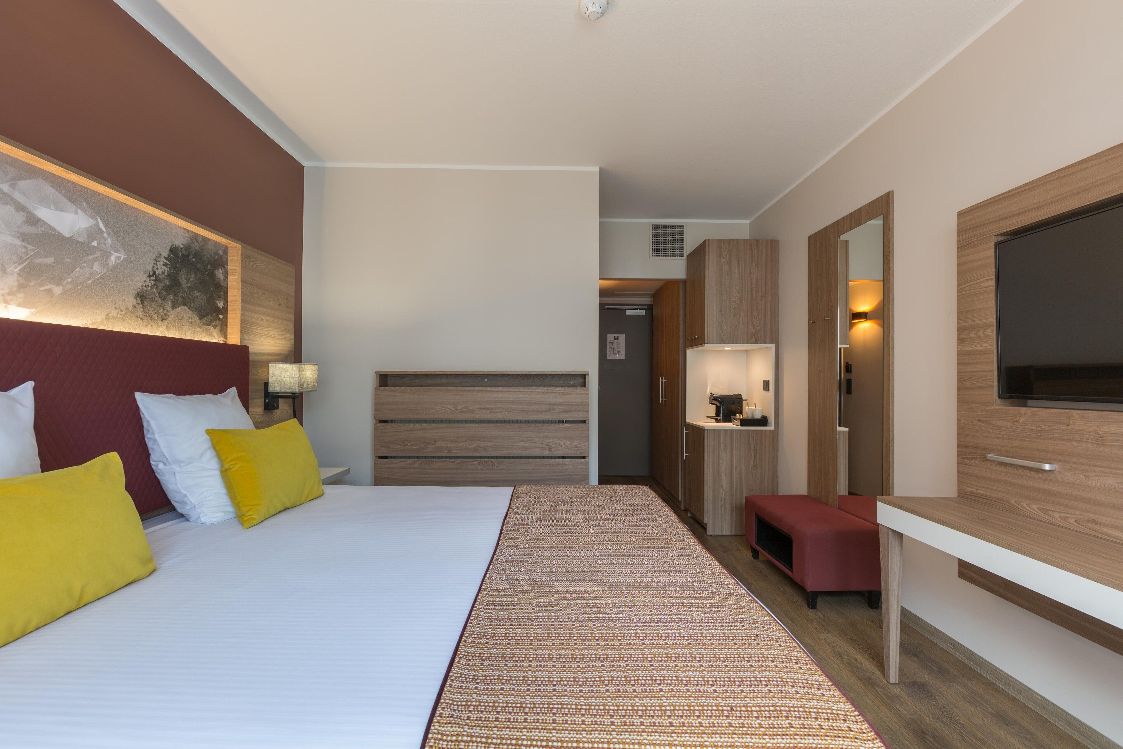 Een moderne hotelkamer met een groot bed, een flatscreen-tv, een houten hoofdbord en een klein zithoekje.