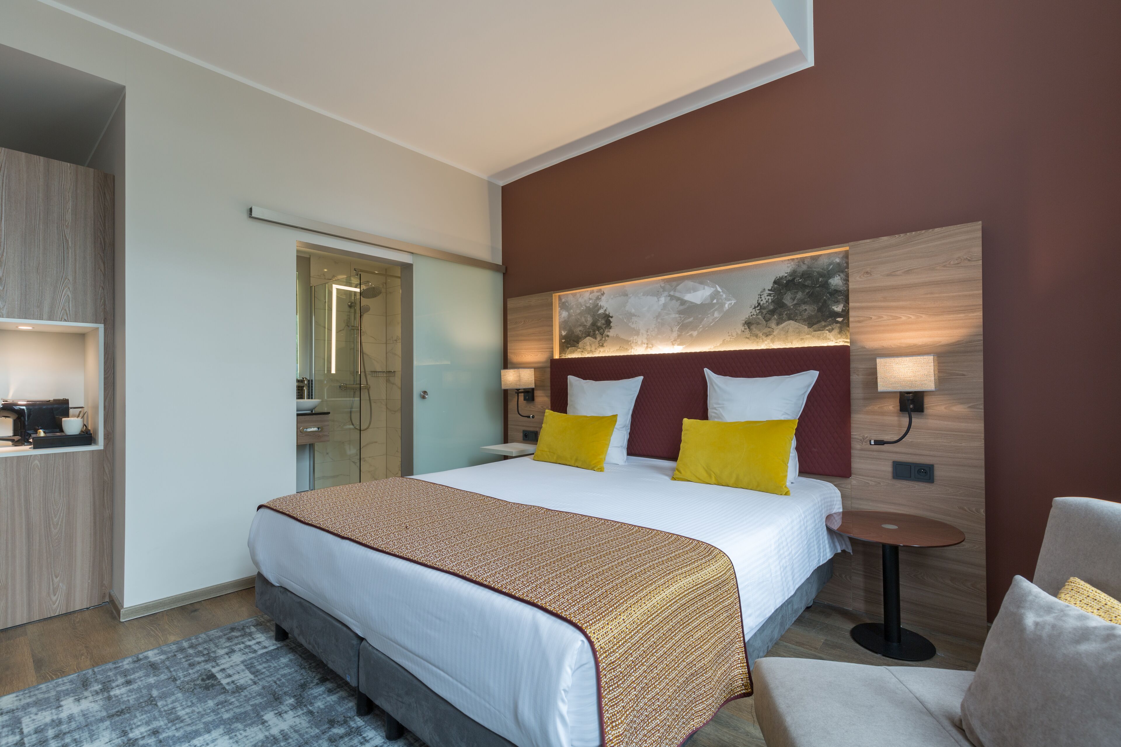 A modern hotel room with a large bed, bedside tables, a small round table, and a seating area.