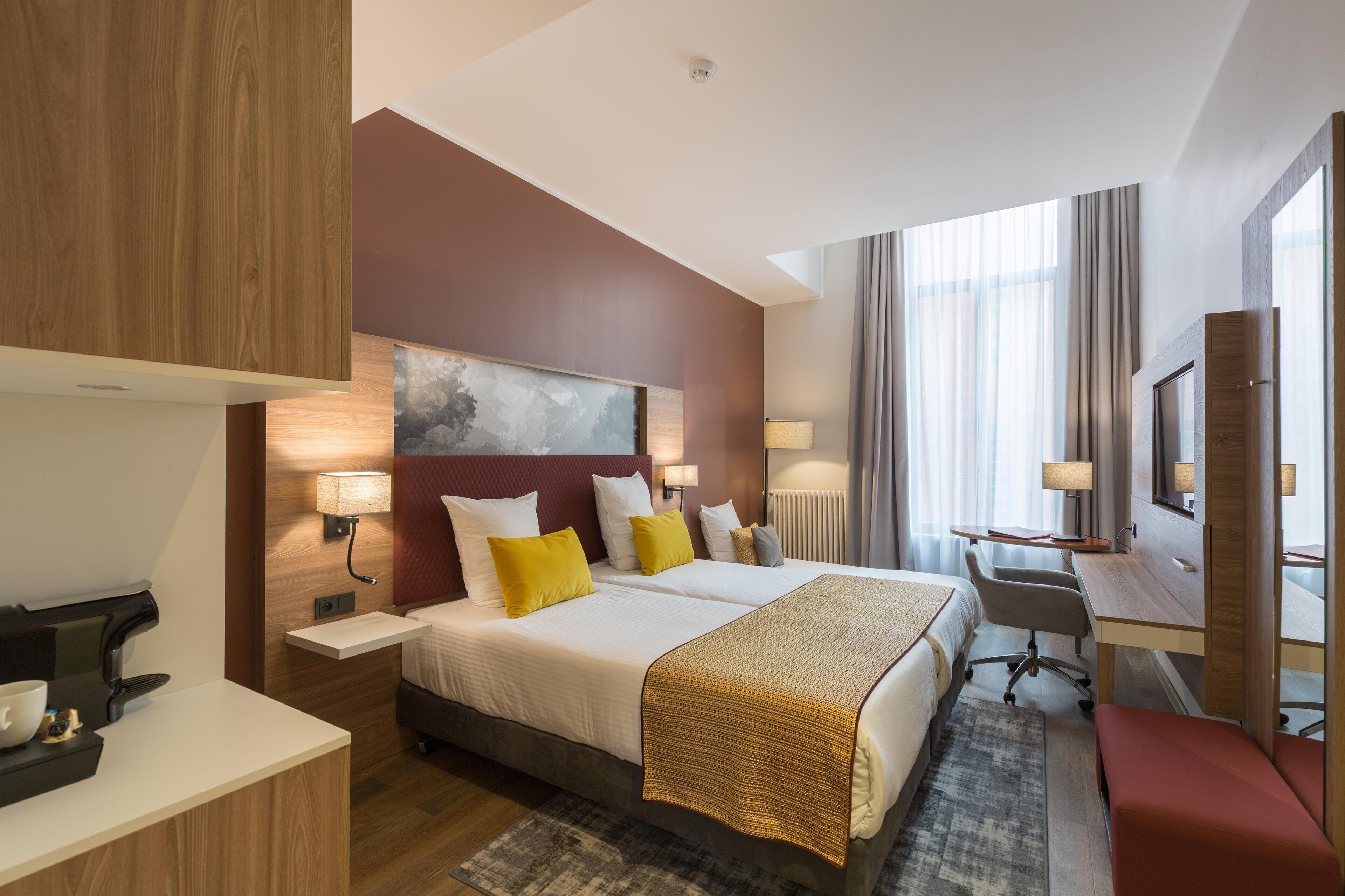A hotel room with a large bed, bedside tables, a desk, a chair, and a television.