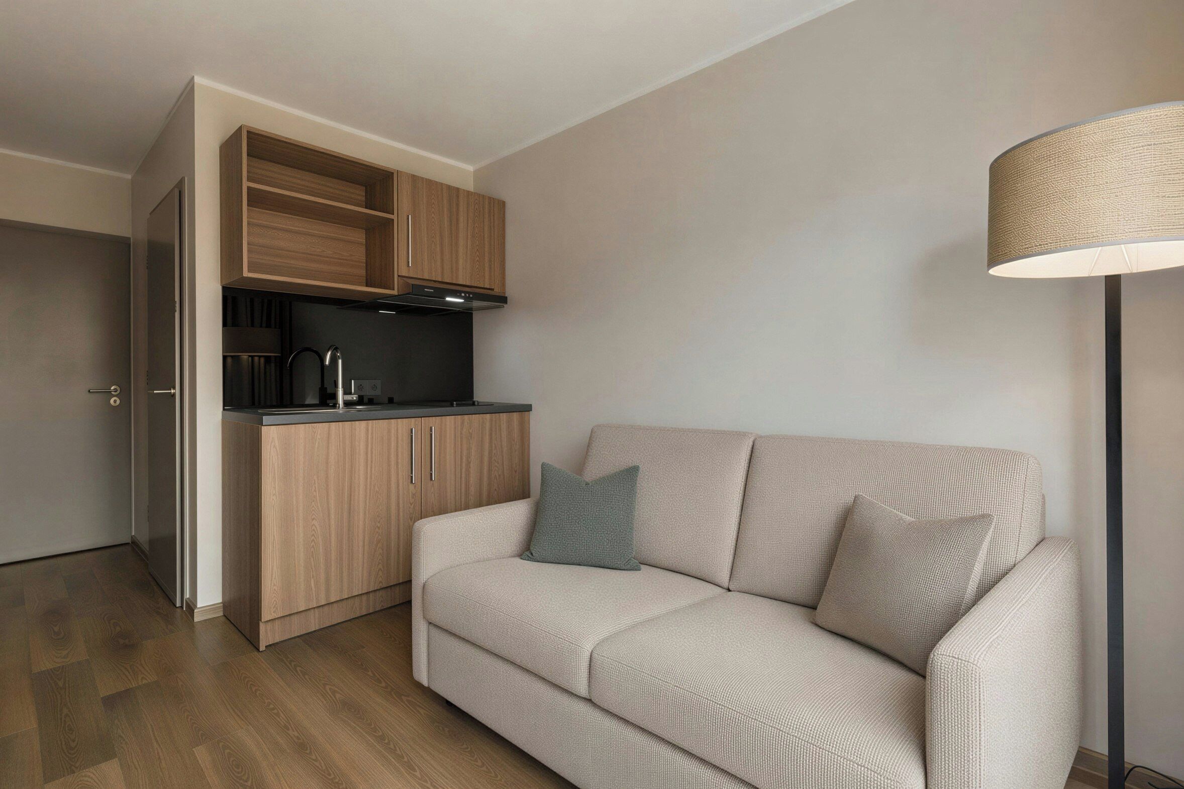 A compact living space with a kitchenette, a sofa with cushions, and a floor lamp.