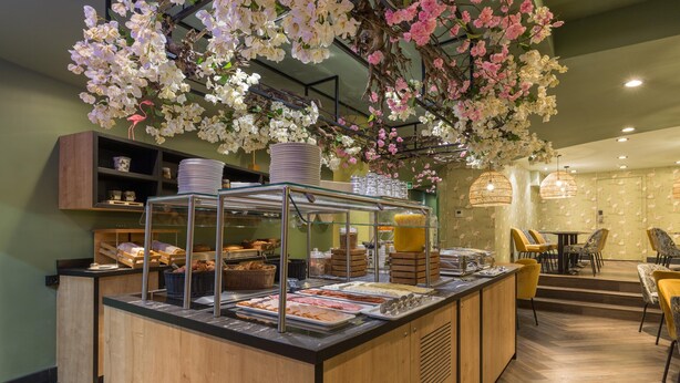 A breakfast bar with a variety of food items, a wooden counter, and hanging floral decorations. - Leonardo Hotel Antwerp (Antwerp)