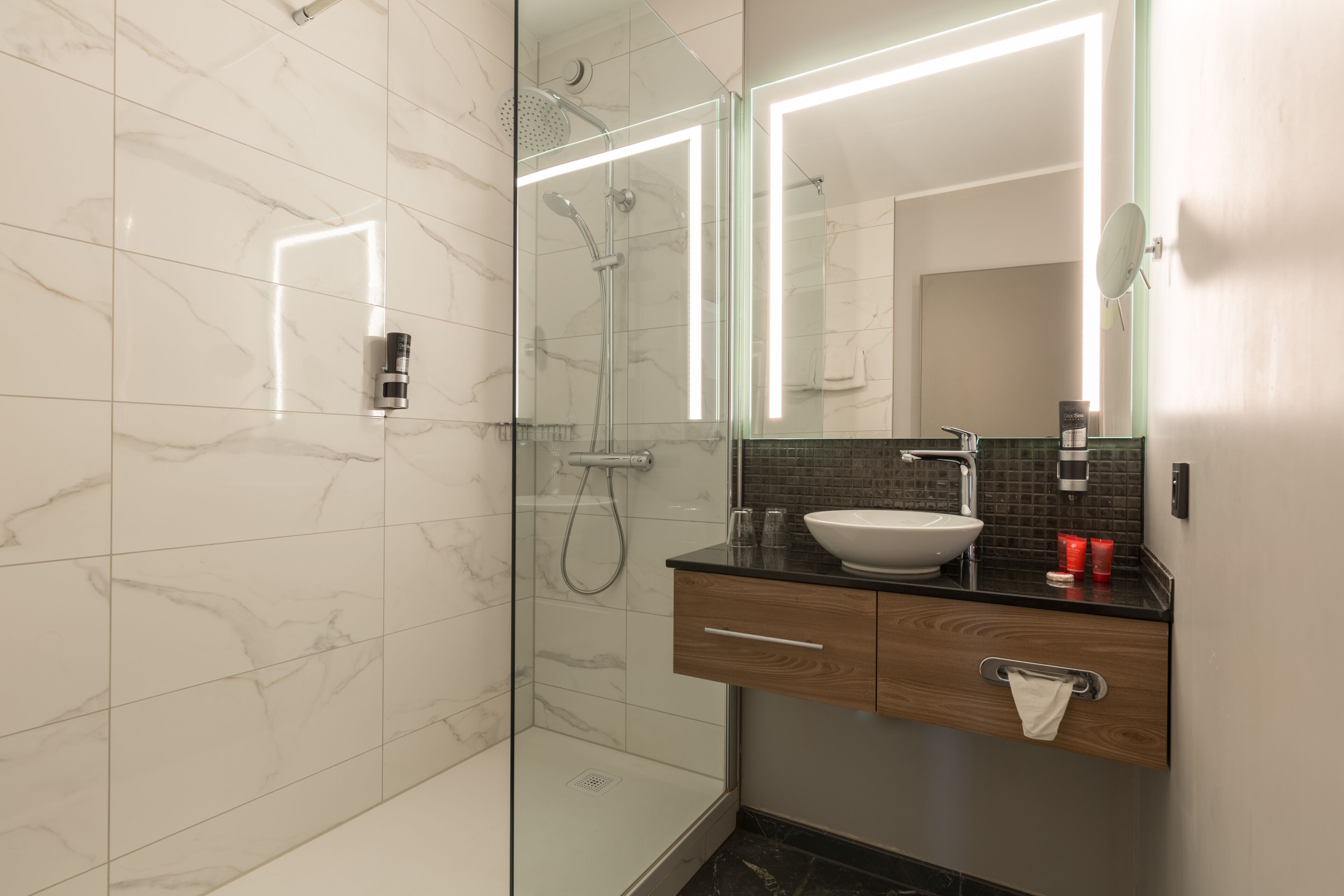 A modern bathroom with a glass-enclosed shower, a sink with a wooden vanity, and a mirror with integrated lighting.