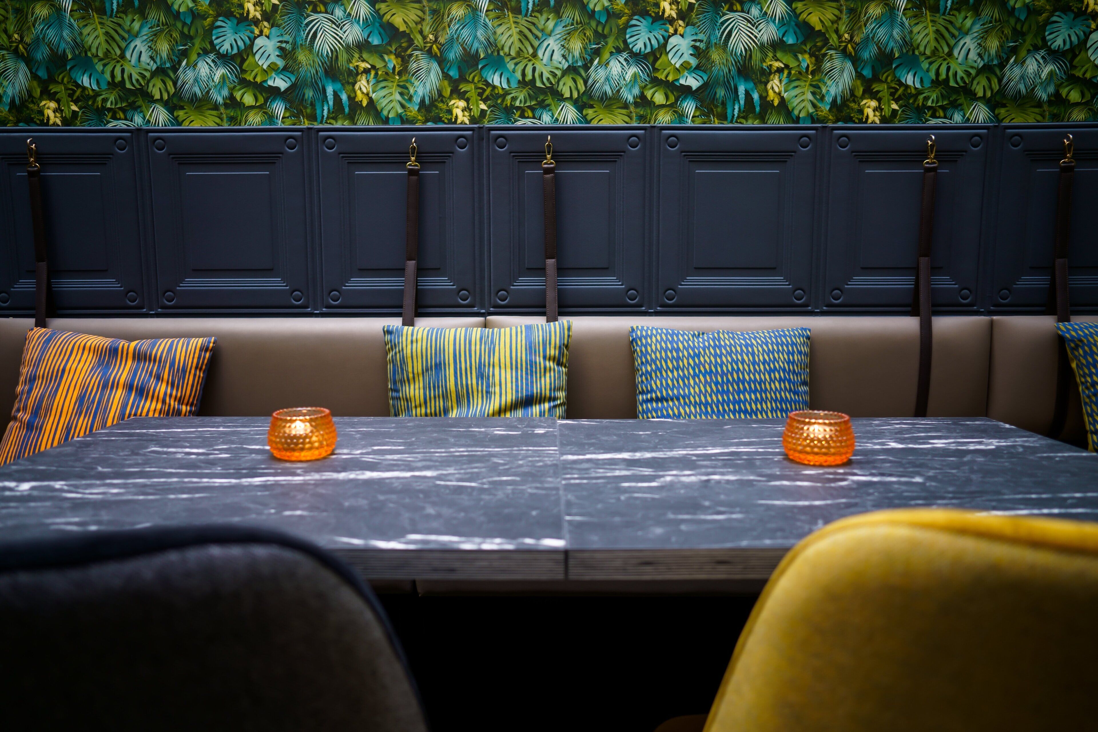 Un restaurante con asientos tipo cabina, una mesa de mármol y una pared decorativa con follaje.