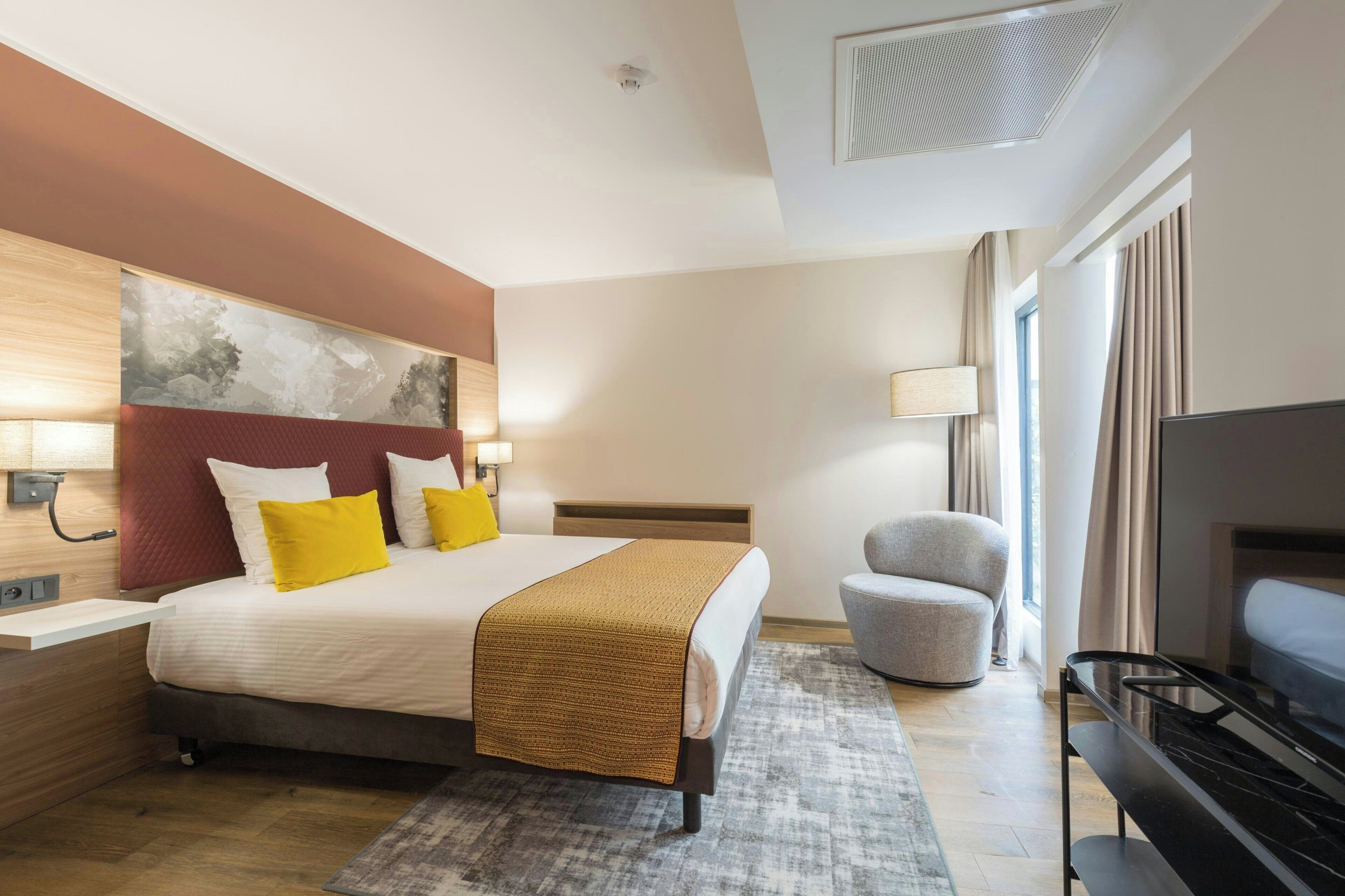 Une chambre d’hôtel avec un lit, une télévision, une chaise et un bureau avec une lampe.