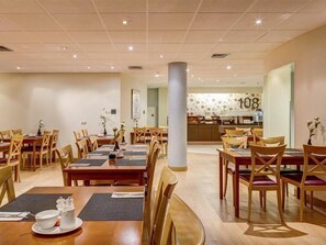 A hotel dining area with multiple tables and chairs, a visible kitchen area in the background, and a number '108' on the wall. - Fletcher Stadshotel Den Haag (The Hague)