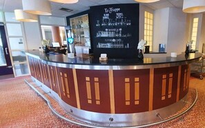 A reception desk with a black sign listing hotel amenities, a glass display case, and a patterned carpet. - Fletcher Stadshotel Den Haag (The Hague)
