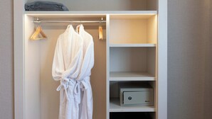 A walk-in closet with a robe hanging, a shelf with a box, and a folded blanket on the top shelf. - Tres Torres Atiram Hotel (Barcelona)