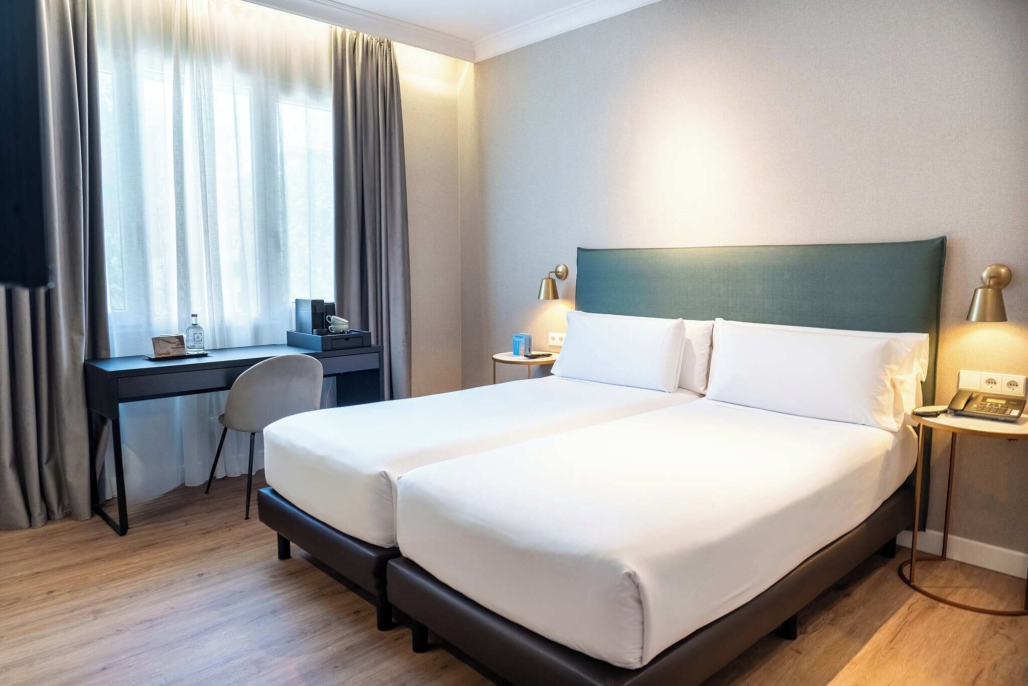Quarto de hotel com cama de casal, escrivaninha, cadeira e mesa pequena com abajur.