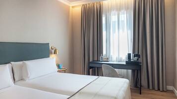 Una habitación de hotel con cama, escritorio, silla y ventana con cortinas.