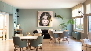 A modern dining area with a large painting, a black sofa, and a dining table with chairs. - Tres Torres Atiram Hotel (Barcelona)