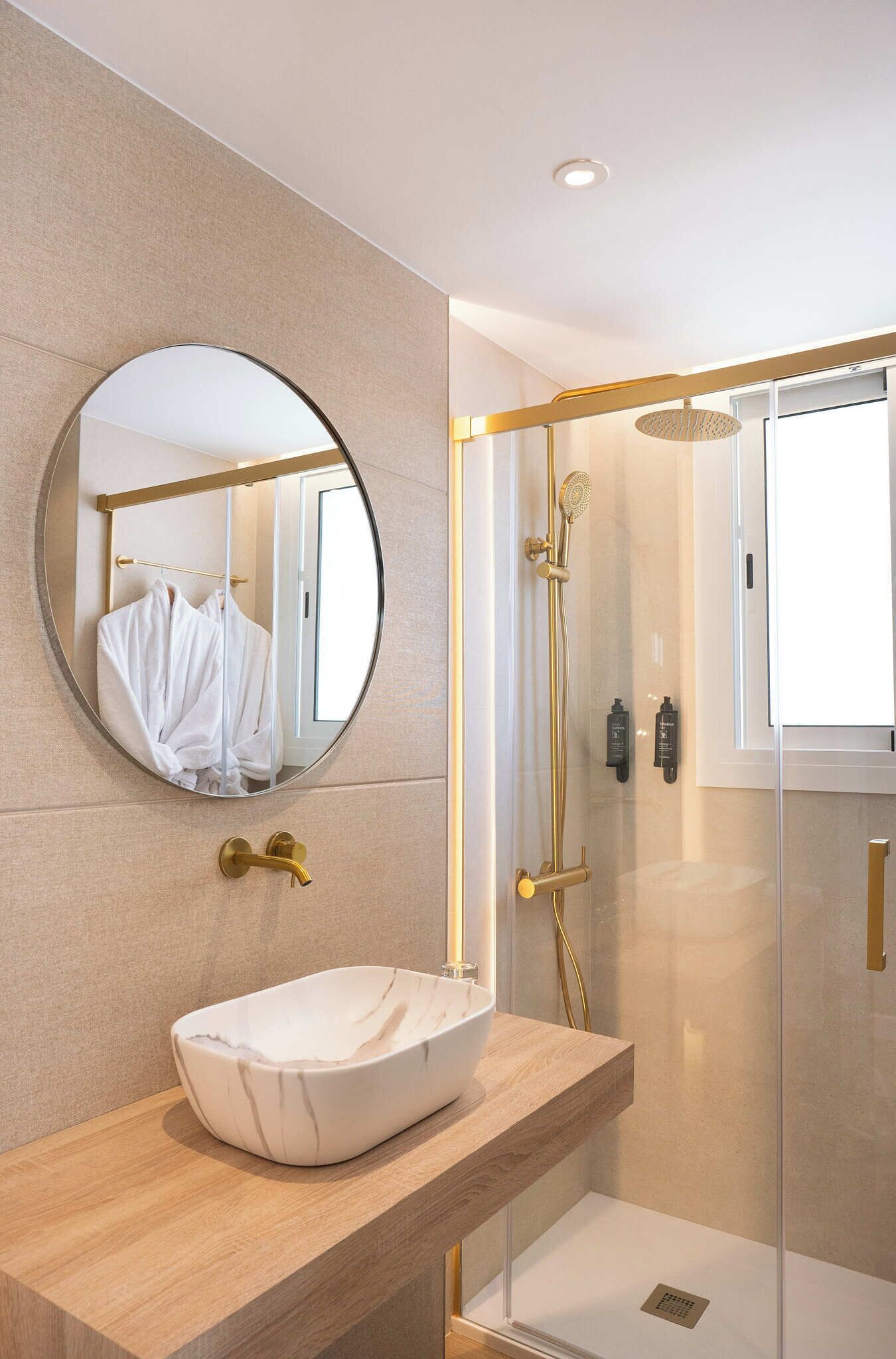 A modern bathroom with a round mirror, a white sink, and a glass-enclosed shower area.
