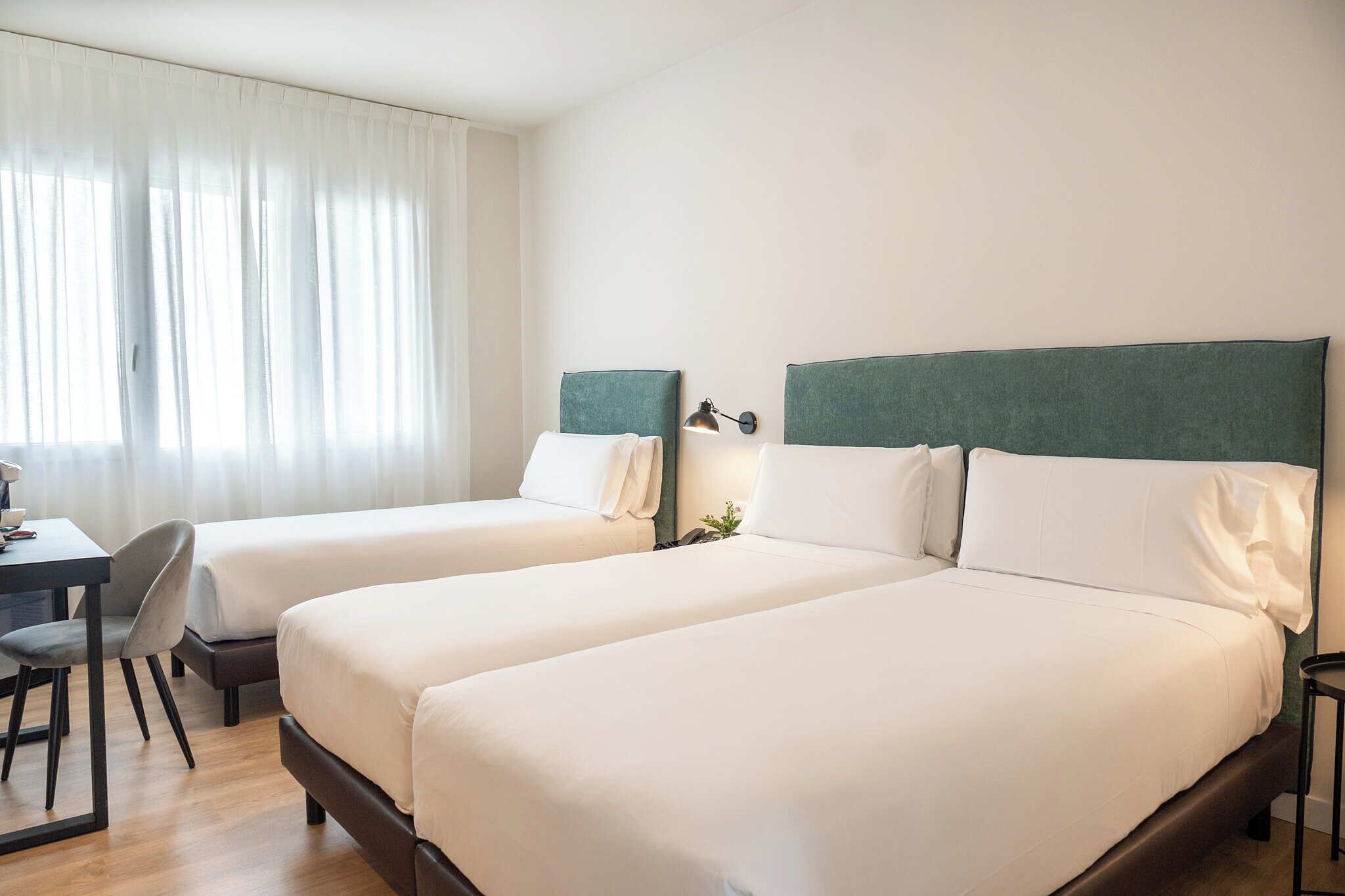 Une chambre d’hôtel avec deux lits simples, un bureau et une chaise.