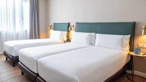 A hotel room with two beds, each with white linens and green headboards. There are bedside lamps and a small table with a book and a phone. - Tres Torres Atiram Hotel (Barcelona)