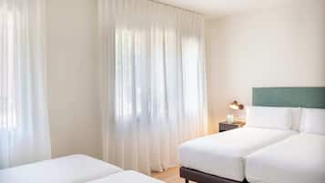 A hotel room with two beds, a nightstand with a lamp, and sheer curtains.