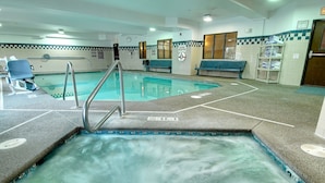 Une piscine avec un escalier en métal, des bancs bleus et un mur carrelé orné d’un motif à carreaux.