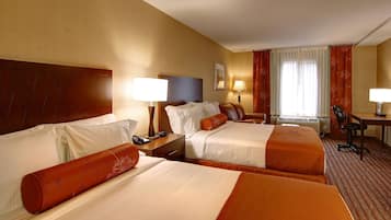 Ein Hotelzimmer mit zwei Betten, einem Schreibtisch, einem Stuhl und einem fensterbepflanzten Fenster.