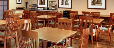 A dining area with wooden tables and chairs, framed artwork on the walls, and a buffet station.