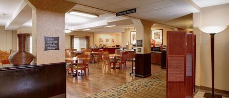 Una hall d'albergo con area ristorazione, reception e indicazione della zona per la colazione continentale.