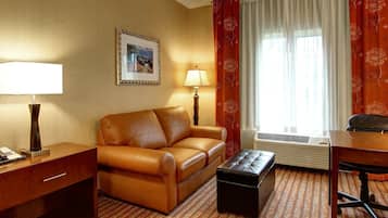 Habitación de hotel con sofá de cuero, una mesita, lámpara, un cuadro en la pared y ventana con cortinas.