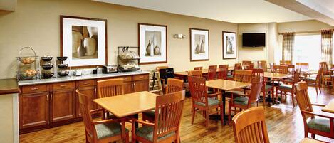 A dining area with wooden tables and chairs, a buffet counter with food items, and framed artwork on the walls.