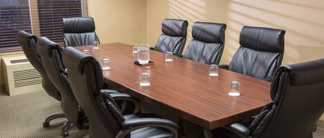Un salón de conferencias con una mesa de madera, sillas de cuero negro y una ventana con persianas.