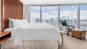 A hotel room with a large bed, a wooden headboard, a city view, a sofa, and an ottoman. - Embarc Vancouver (Vancouver)