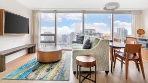A modern living room with a large window, a flat-screen TV, a round coffee table, a sofa, and a dining area with wooden chairs and a table. - Embarc Vancouver (Vancouver)