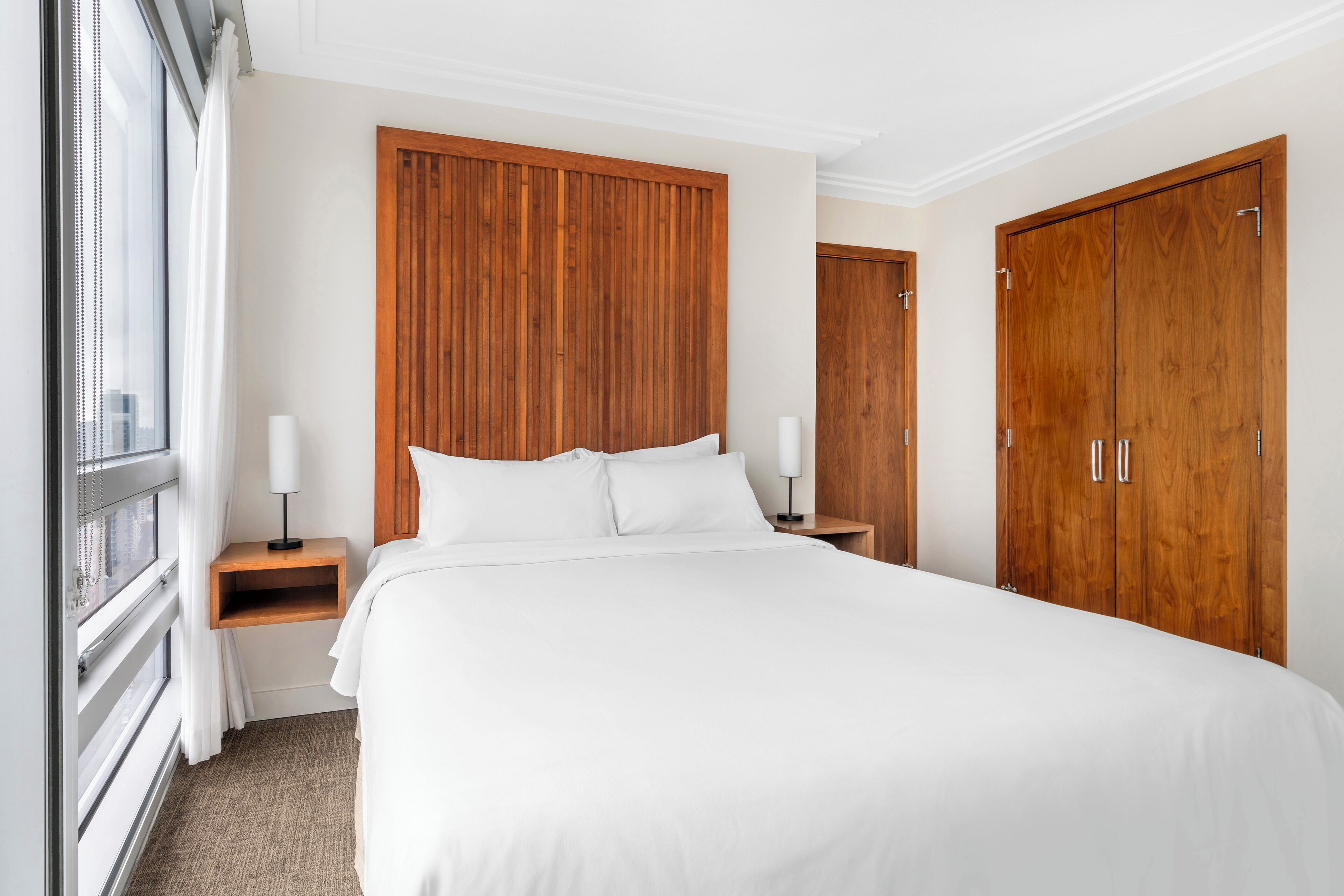 A hotel room with a large bed, wooden wardrobe, and a nightstand with a lamp.