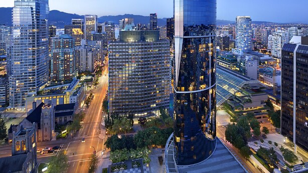 A cityscape at dusk with modern high-rise buildings, a prominent curved skyscraper, and a historic church. - Embarc Vancouver (Vancouver)