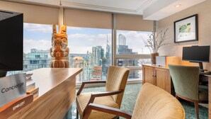A hotel room with a desk, a chair, a television, and a large window offering a city view. - Embarc Vancouver (Vancouver)