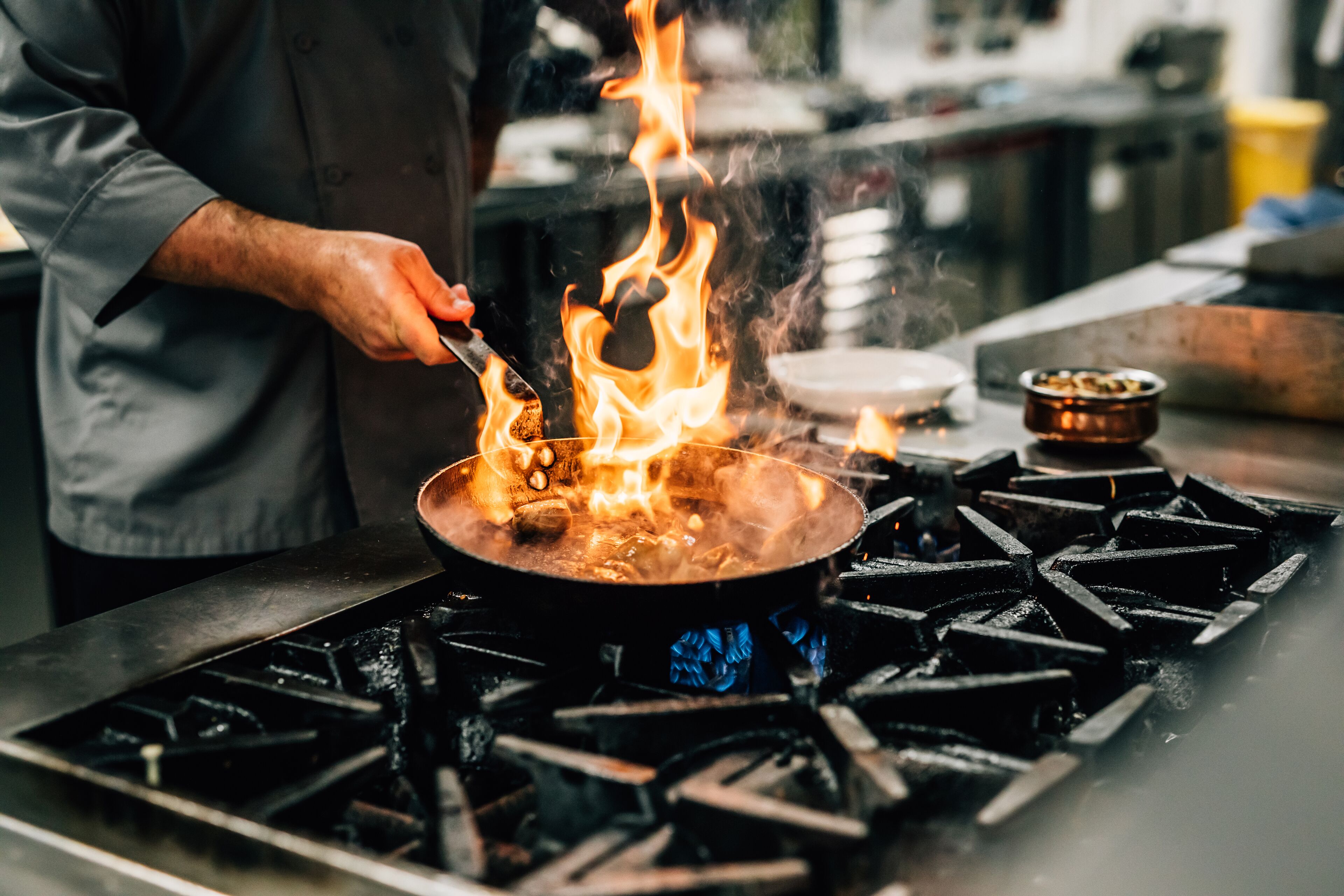 A chef cooking with flames on a stove in a kitchen.
