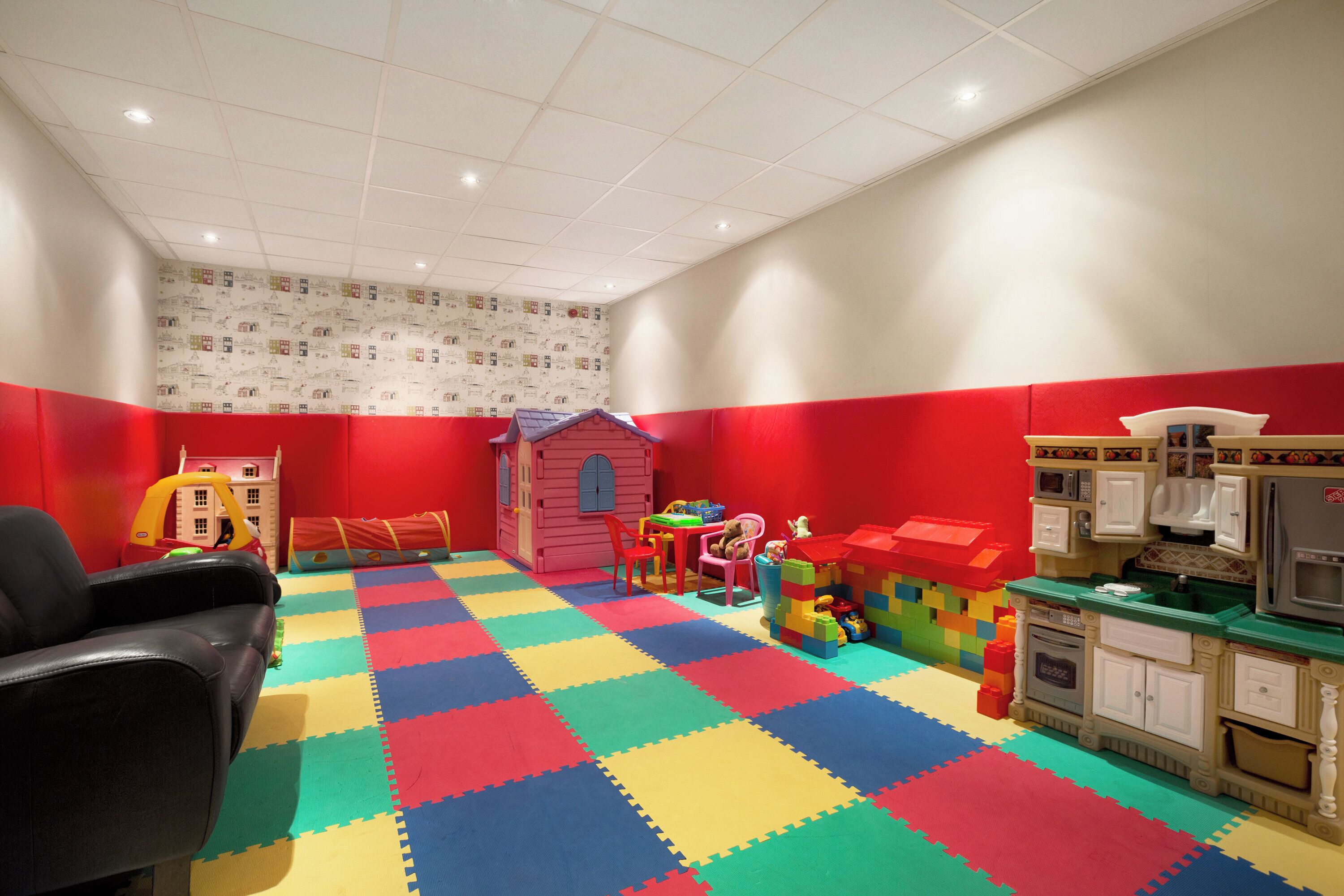 A playroom with a colorful foam floor, a playhouse, and a toy kitchen.