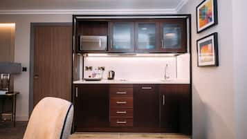 A compact kitchen with dark wood cabinets, a white countertop, and a microwave. There are two framed artworks on the wall.