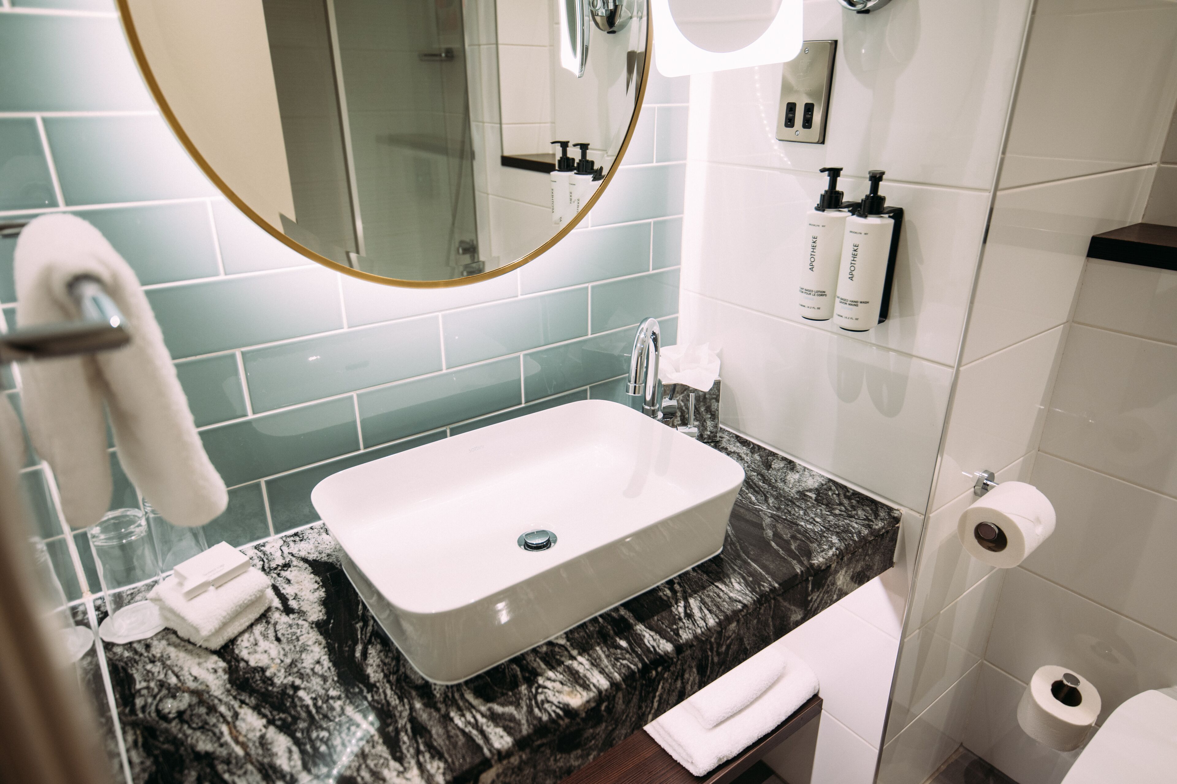 A bathroom with a white sink, marble countertop, and a mirror with a gold frame.