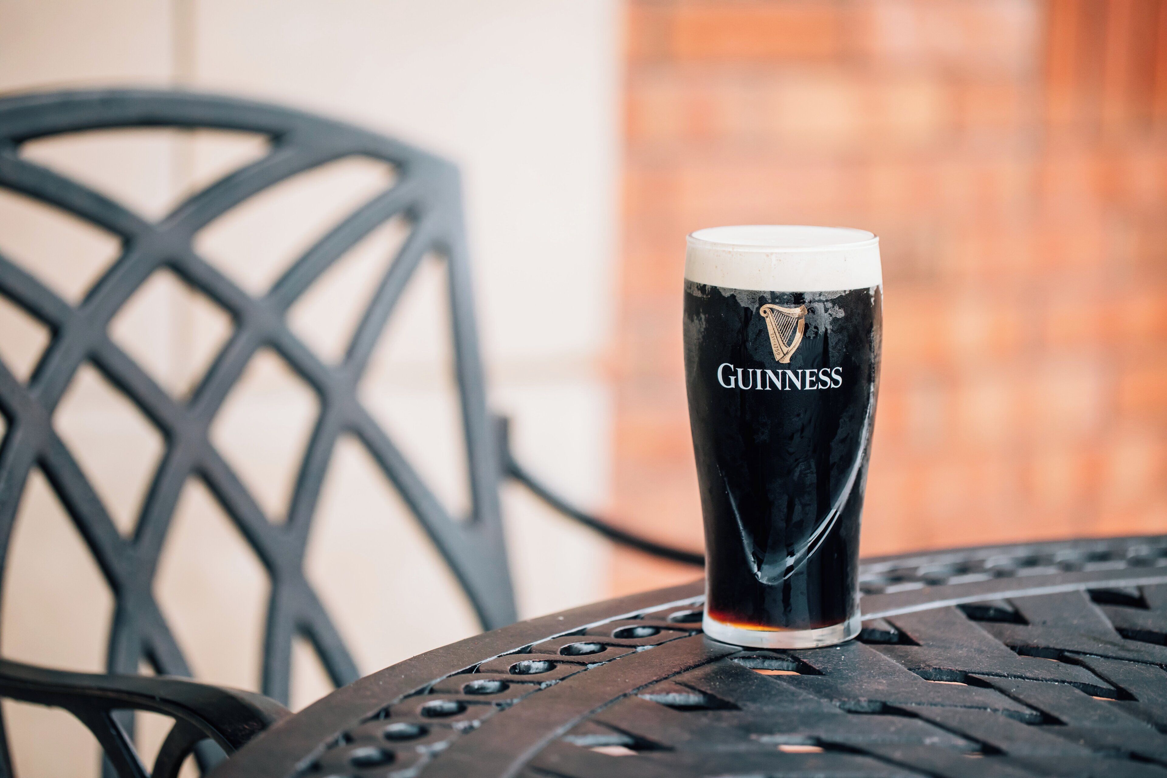 Un vaso de Guinness sobre una mesa metálica, con una silla al fondo.