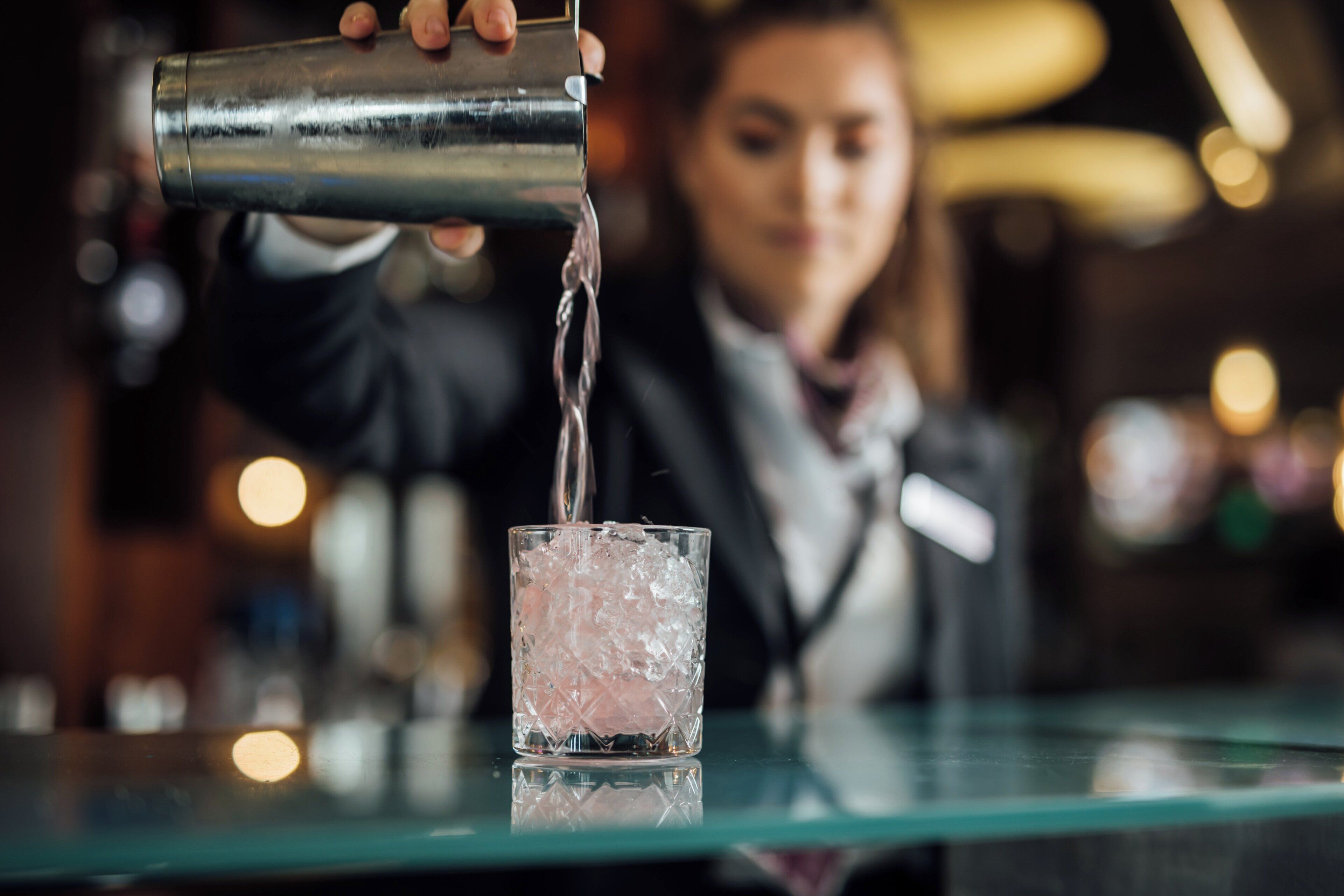 A bartender pouring a drink into a glass with ice.
