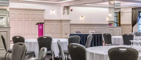 A conference room with round tables, grey chairs, and a podium with a pink sign.