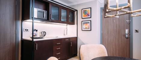 A compact kitchen with dark wood cabinets, a stainless steel microwave, and a modern light fixture.
