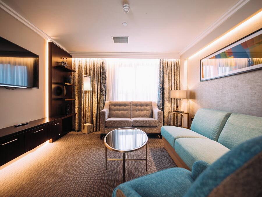 A hotel room with a sofa, armchair, TV, and a painting on the wall.