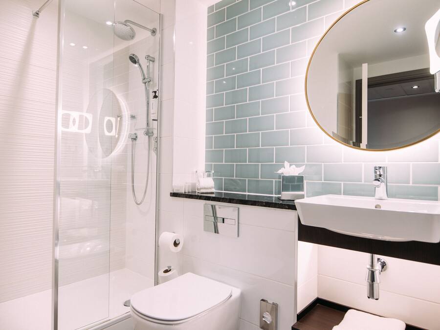Un baño moderno con ducha envuelta en vidrio, inodoro blanco, lavamanos con espejo y pared con azulejos azules.