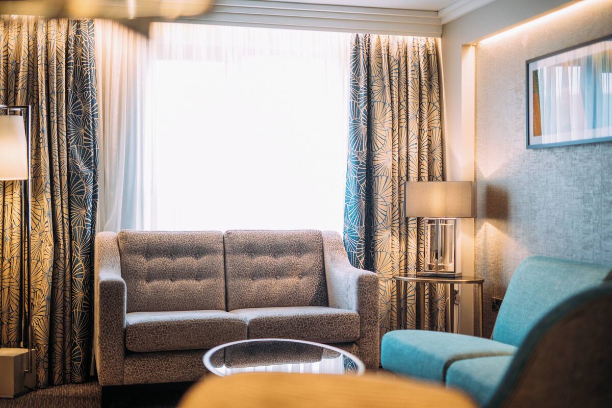 A modern hotel room with a sofa set, a coffee table, and a lamp.