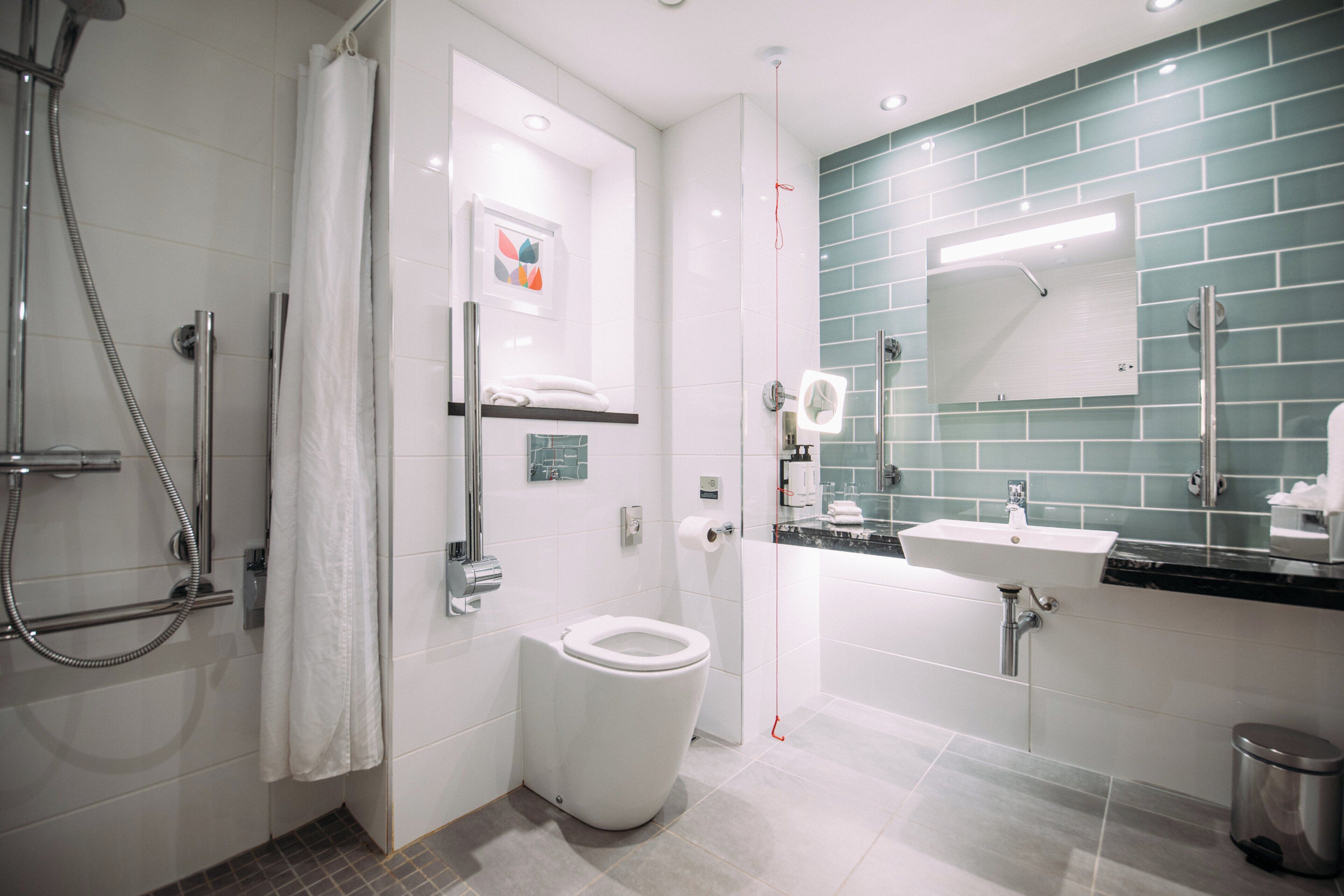 Un baño moderno con ducha, inodoro, lavamanos y un espejo con revestimiento de azulejos verdes.